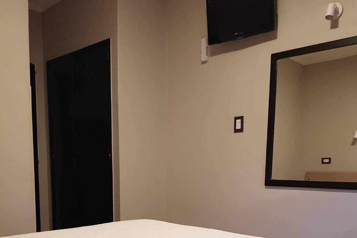 A bedroom with a bed, a TV mounted on the wall, and a door.
