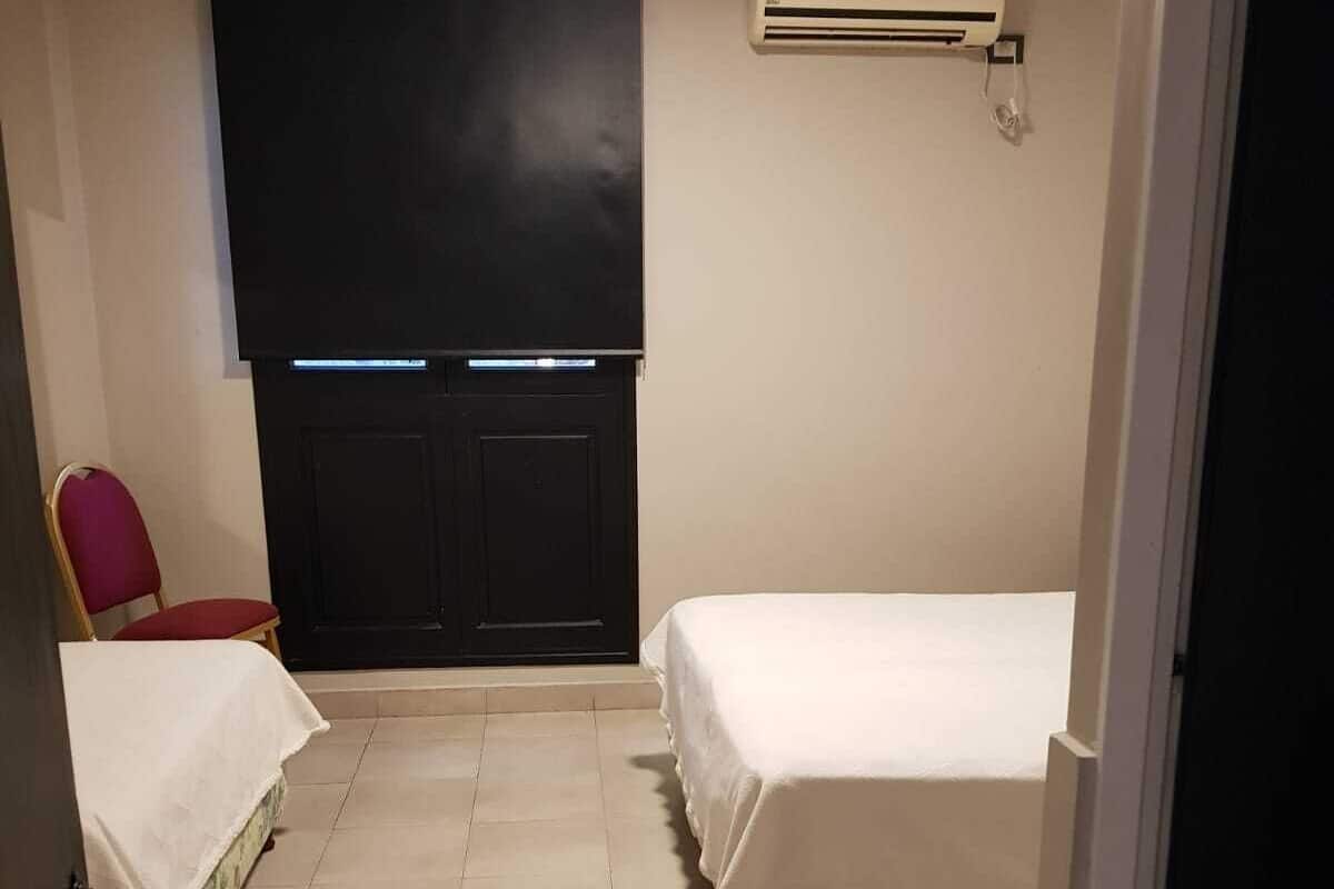 A small, clean room with a bed, a chair, and a window with blinds.