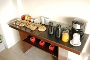 A breakfast buffet setup with various food items, cups, and a coffee machine. - Horizonte Hotel (Mar del Plata)