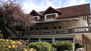 A two-story building with a balcony, a red-tiled roof, and a garden with flowering plants. - Hotel Crismalu (San Martín de los Andes)