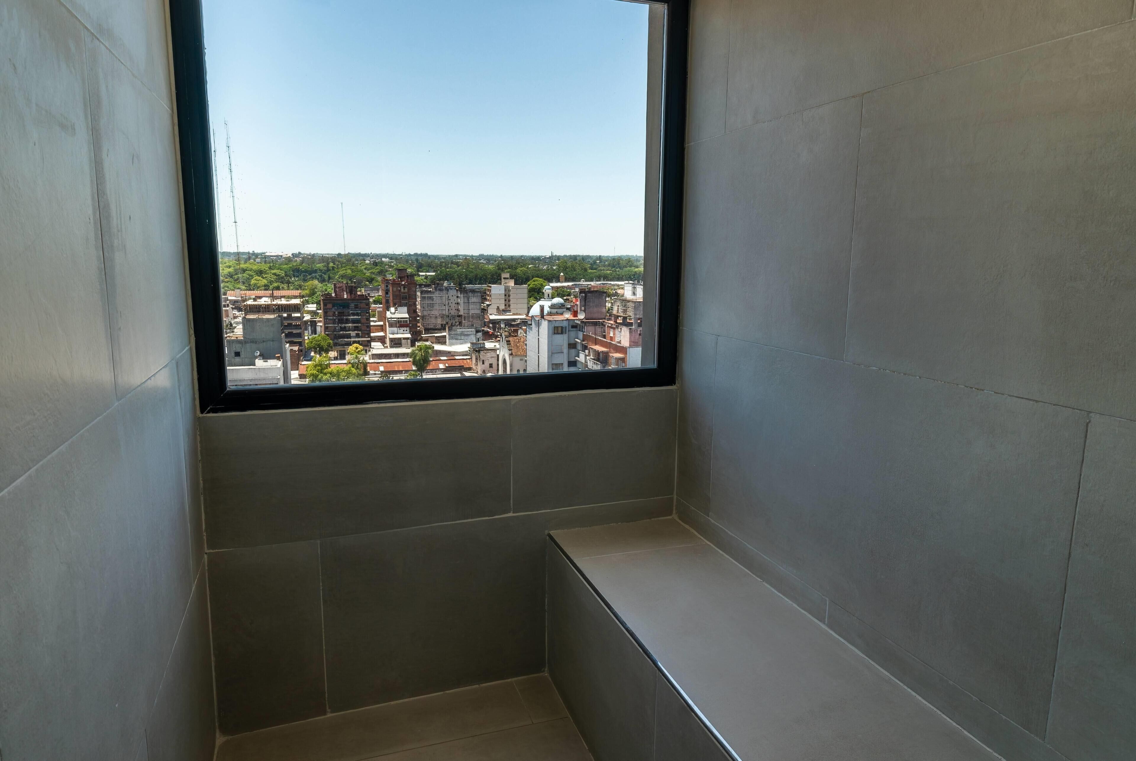 Una habitación con un ventanal grande, paredes con azulejos y un banco.