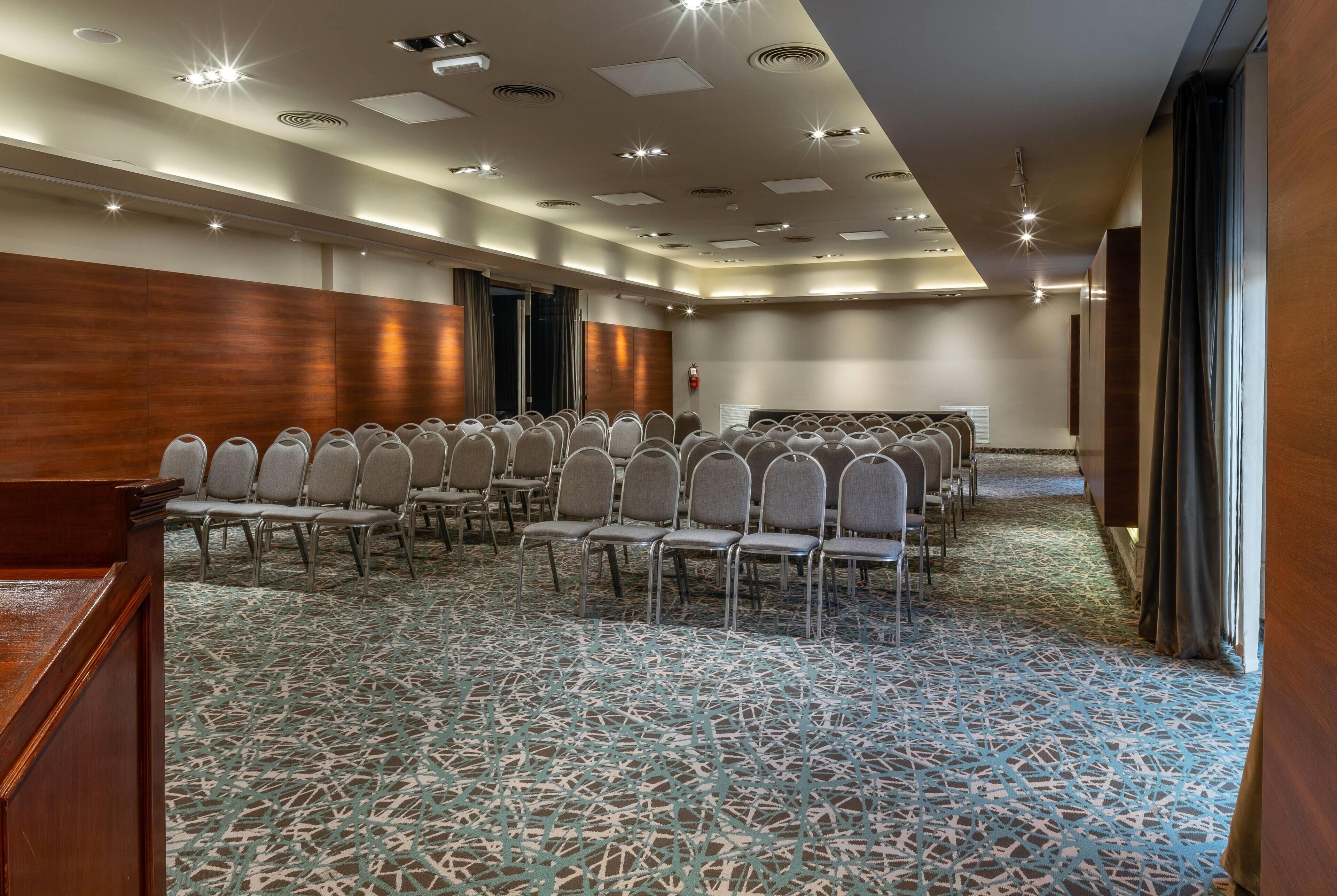 Una sala conferenze con file di sedie, un podio in legno e una moquette decorata.
