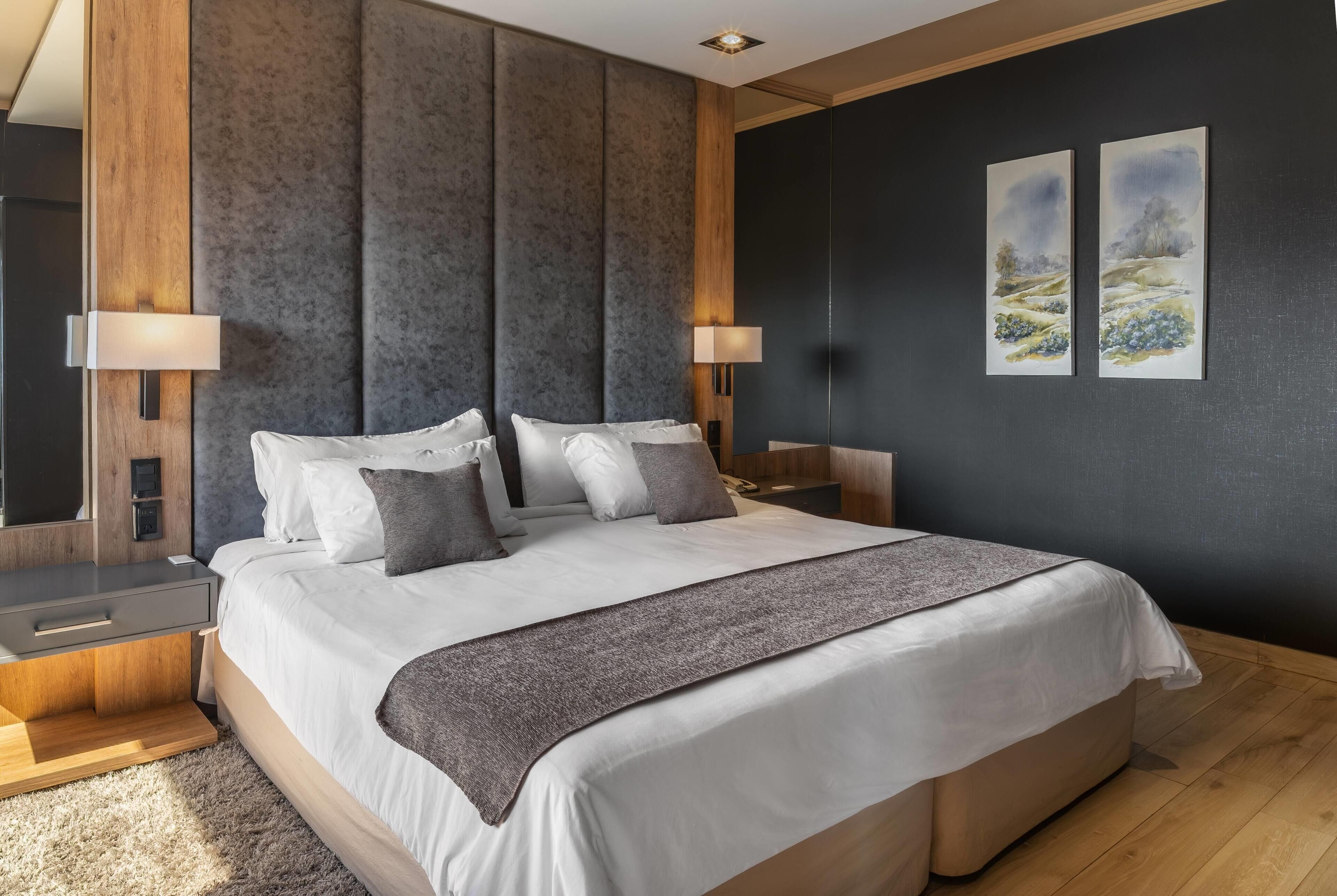 A modern bedroom with a large bed, two bedside tables, a headboard, and two wall-mounted lamps.