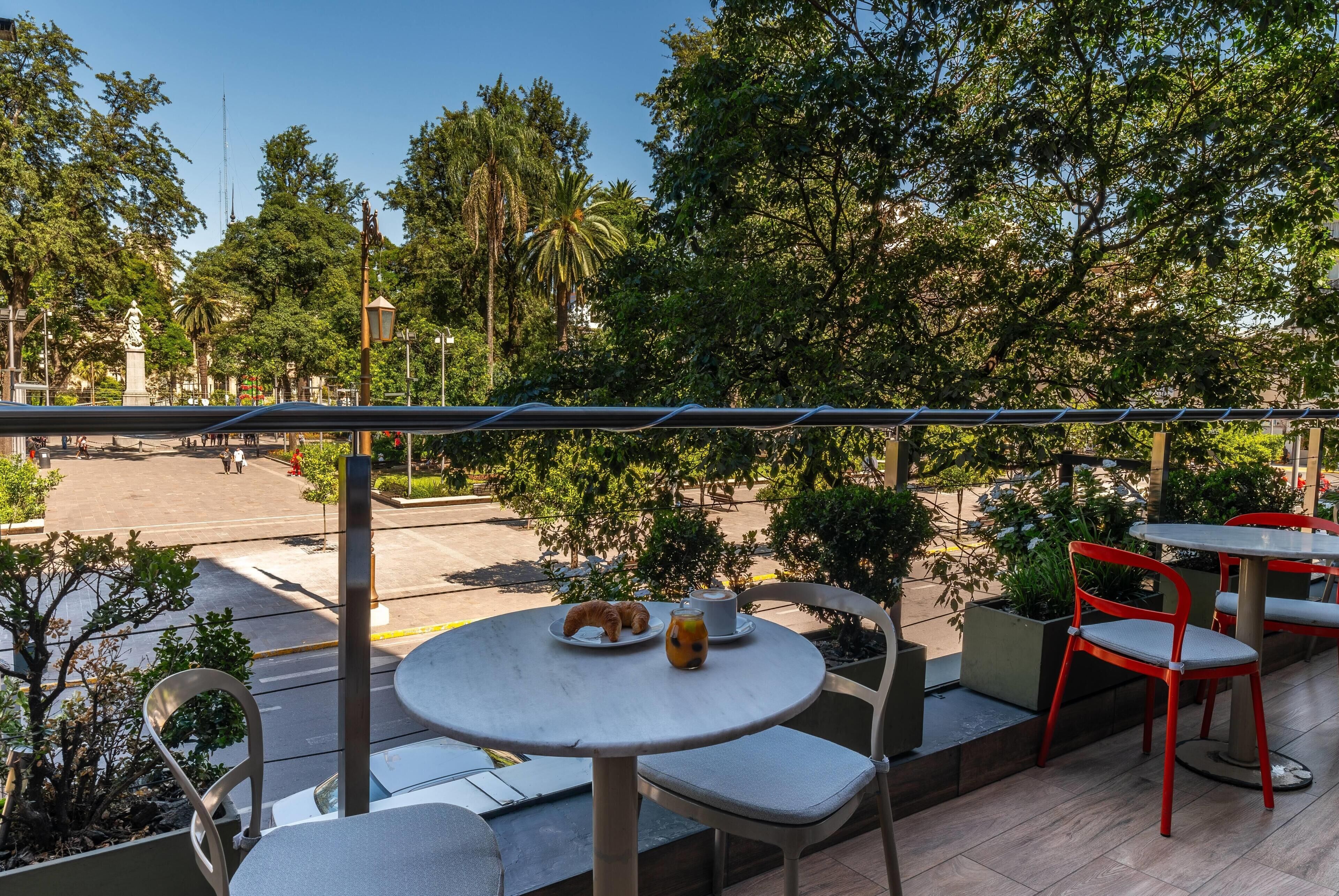 Un café en plein air, avec des tables et des chaises, entouré de verdure et sous un ciel dégagé.