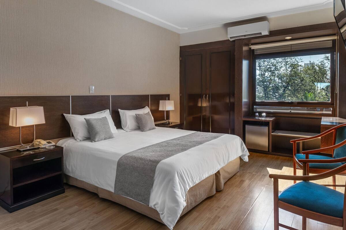A hotel room with a large bed, bedside lamps, a desk, and a chair.