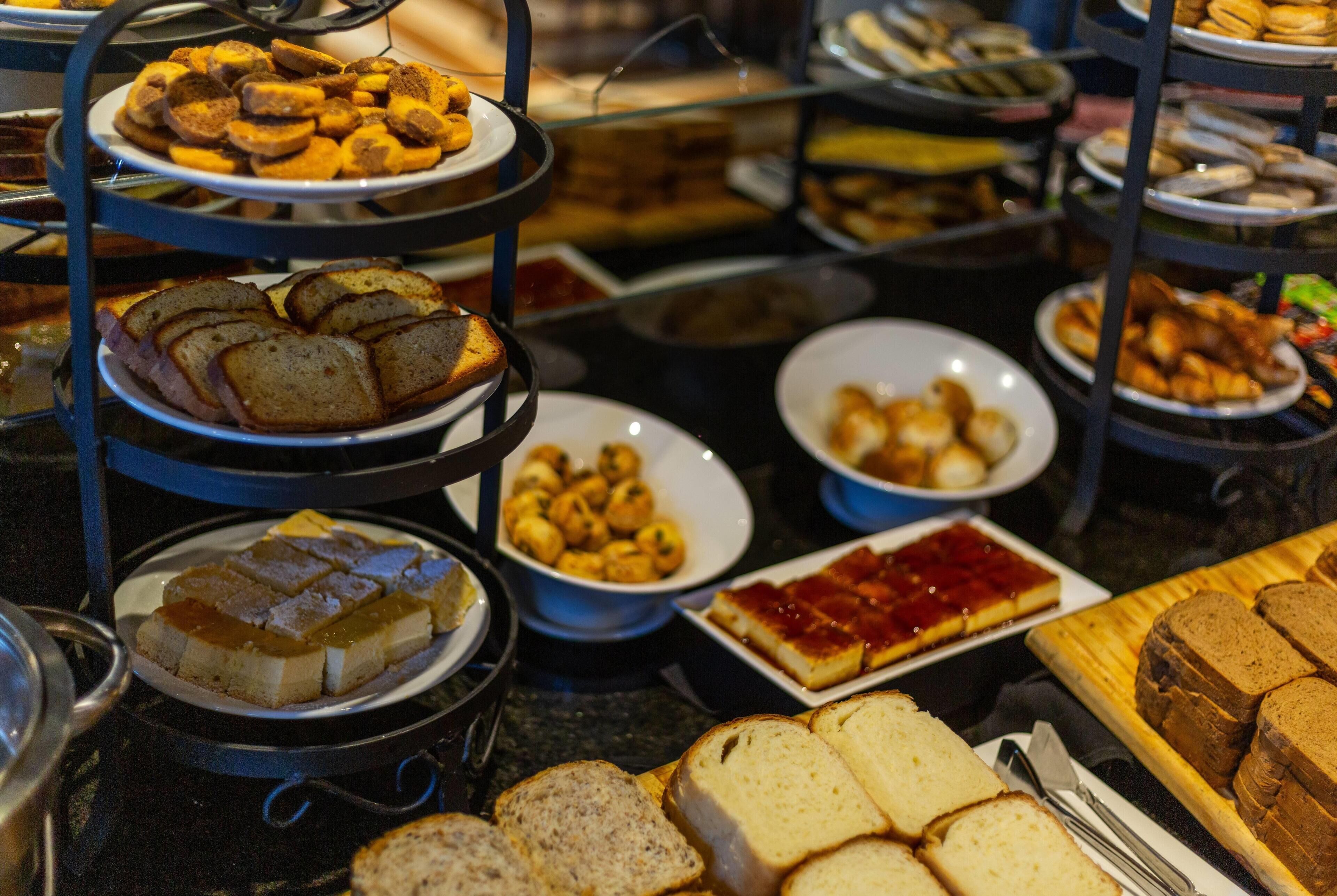 Ein Buffet mit mehreren Tabletts verschiedener Speisen, darunter Brot, Gebäck und Desserts.
