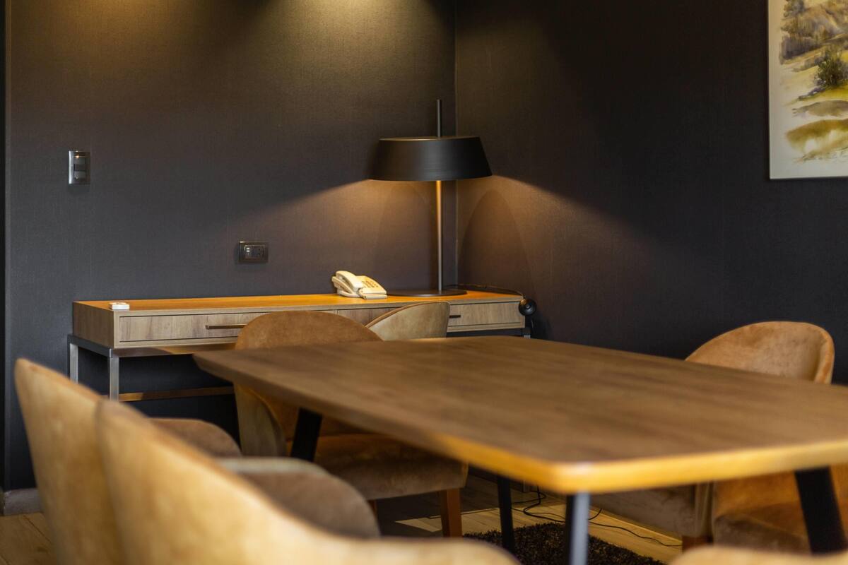 A modern room with a wooden desk, chairs, a lamp, and a painting on the wall.
