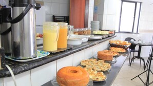 Ein Buffet mit verschiedenen Speisen, darunter Gebäck und eine große Torte, sowie zwei Kännchen Orangensaft.