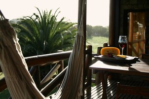 Una mesa de madera con un plato de comida y una copa de vino tinto, con vistas a un exuberante paisaje verde con palmeras.