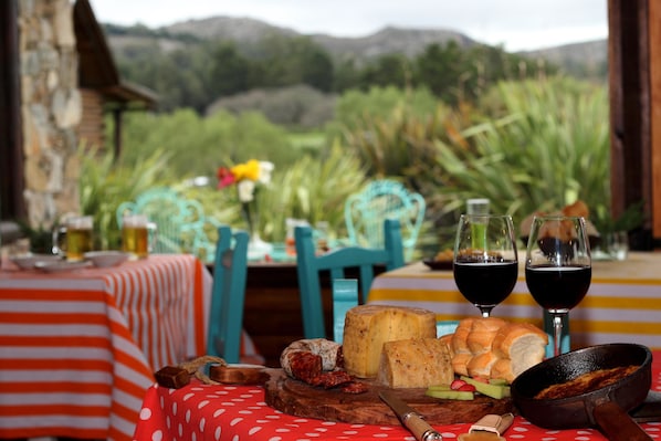 A table with cheese, bread, and wine glasses set against a scenic mountain backdrop.