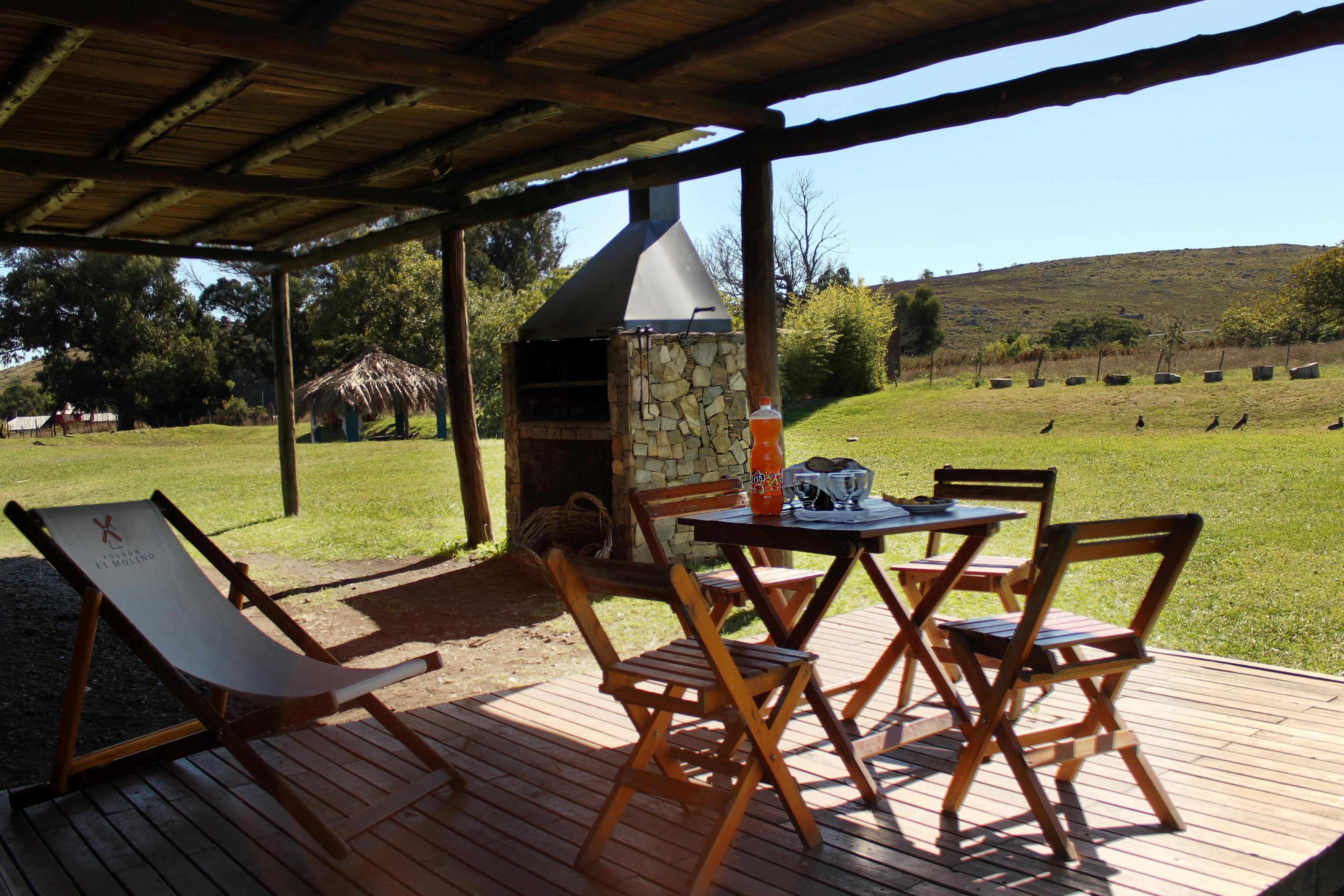 Una terraza de madera con una parrilla de piedra y una mesa con sillas.