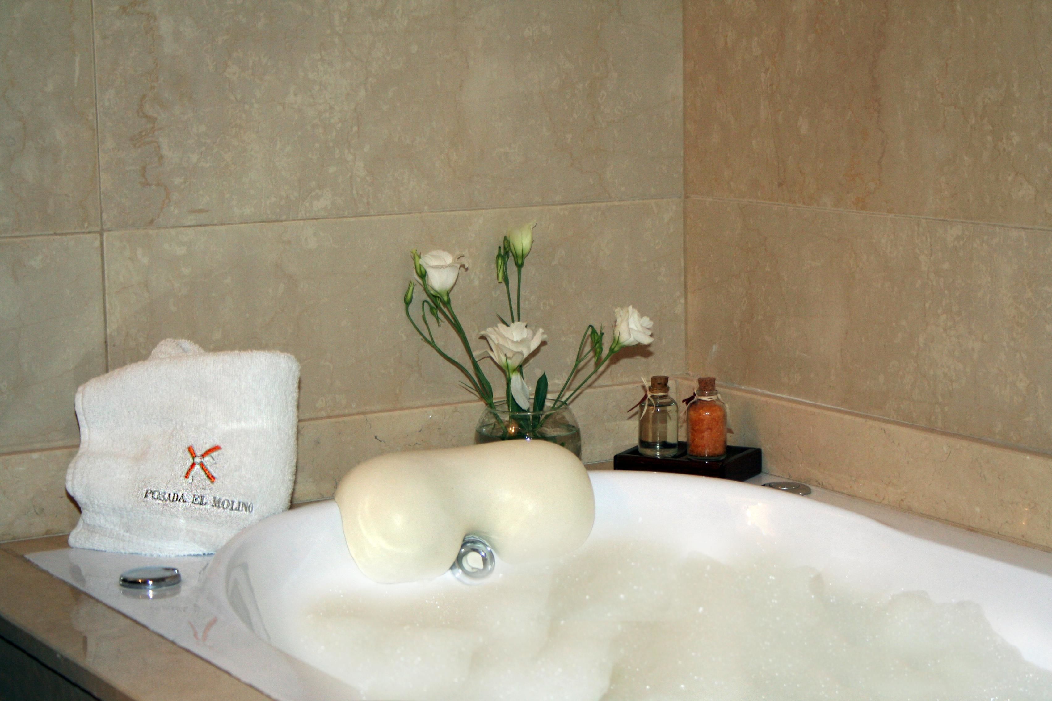 Ein Badezimmer mit einer Badewanne voller Blasen, einem Handtuch und einer kleinen Vase mit Blumen.