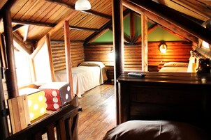 Un dormitorio tipo cabaña de madera con dos camas, paredes de madera, techo inclinado y una ventana que proporciona luz natural.