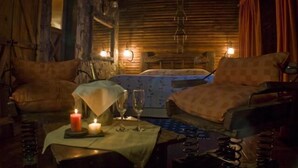 A cozy room with a bed, two chairs, a table with candles and glasses, and a wooden wall. - Posada El Molino (Tandil)