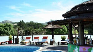 A poolside area with lounge chairs, a bar, and a thatched-roof structure. - Posada El Molino (Tandil)