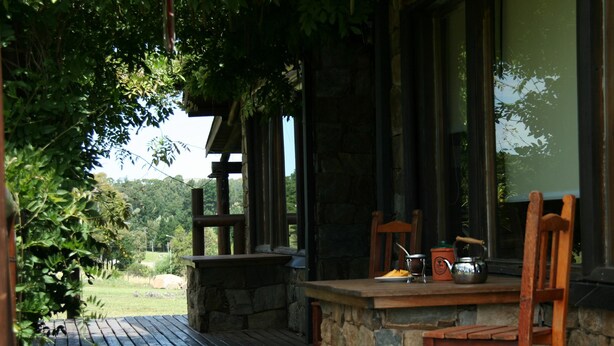 A wooden deck with stone walls, a wooden bench, and a table with a kettle and cup. - Posada El Molino (Tandil)
