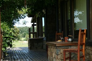 Une terrasse en bois avec des murs en pierre, un banc en bois et une table avec une bouilloire et une tasse.