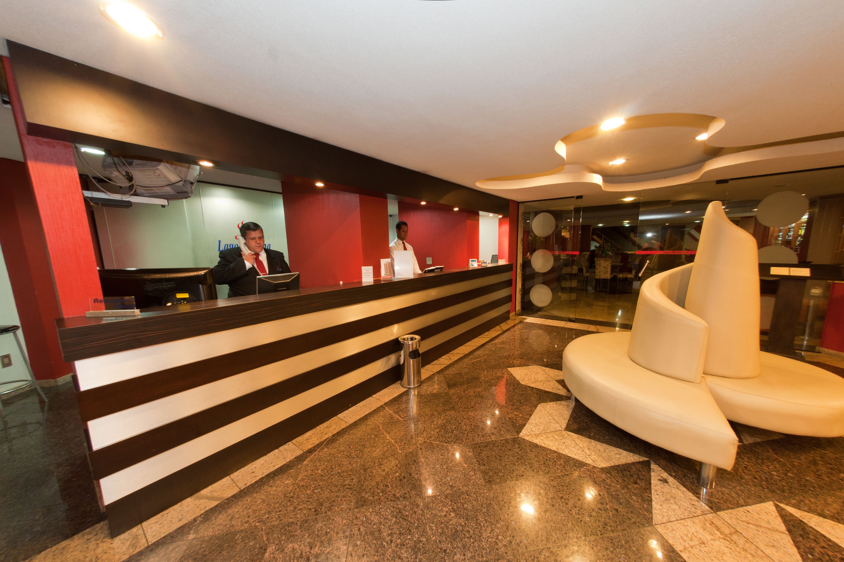 A modern hotel lobby with a reception desk, a seating area, and a glass partition.