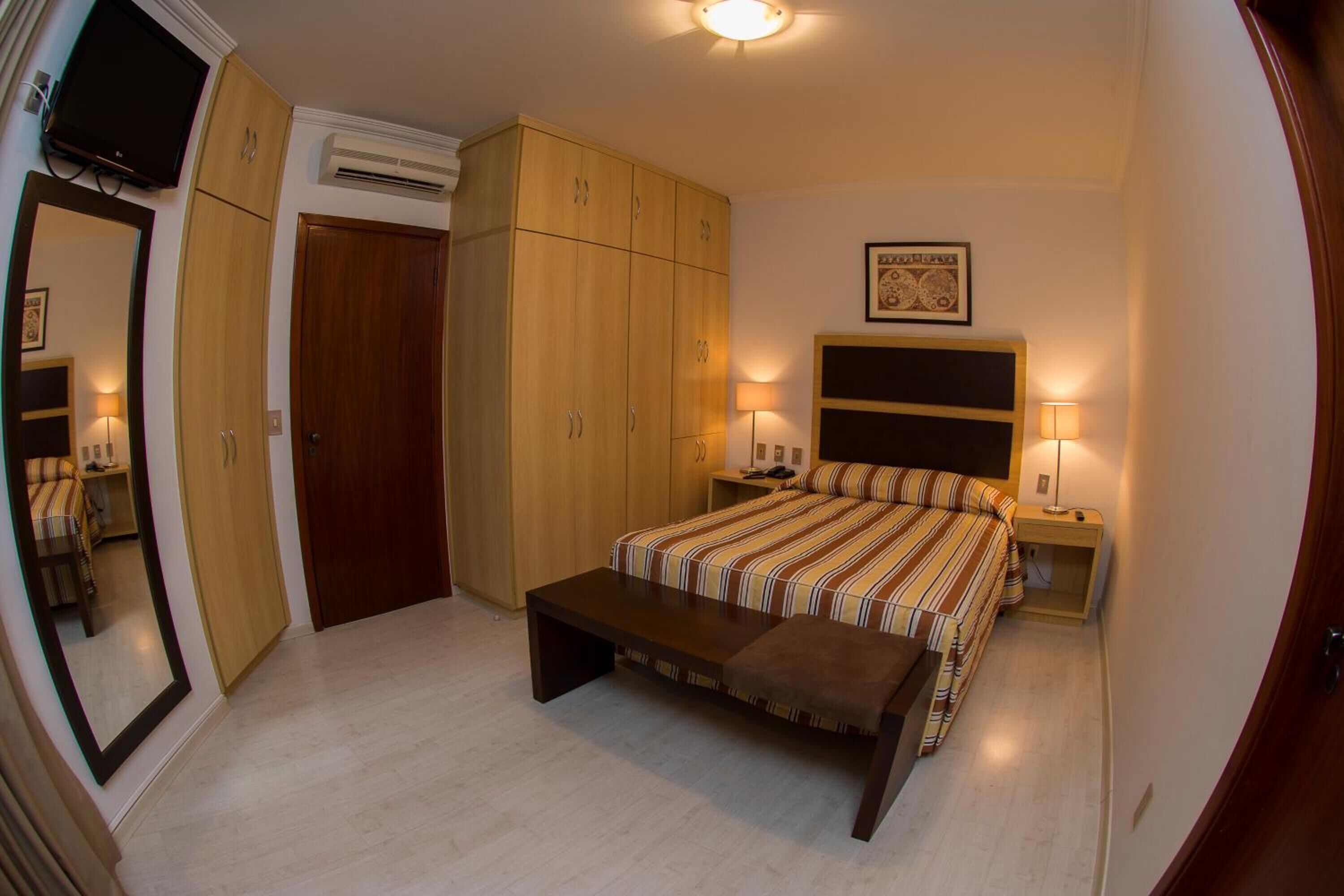 A bedroom with a bed, a bench, a wardrobe, and a television.