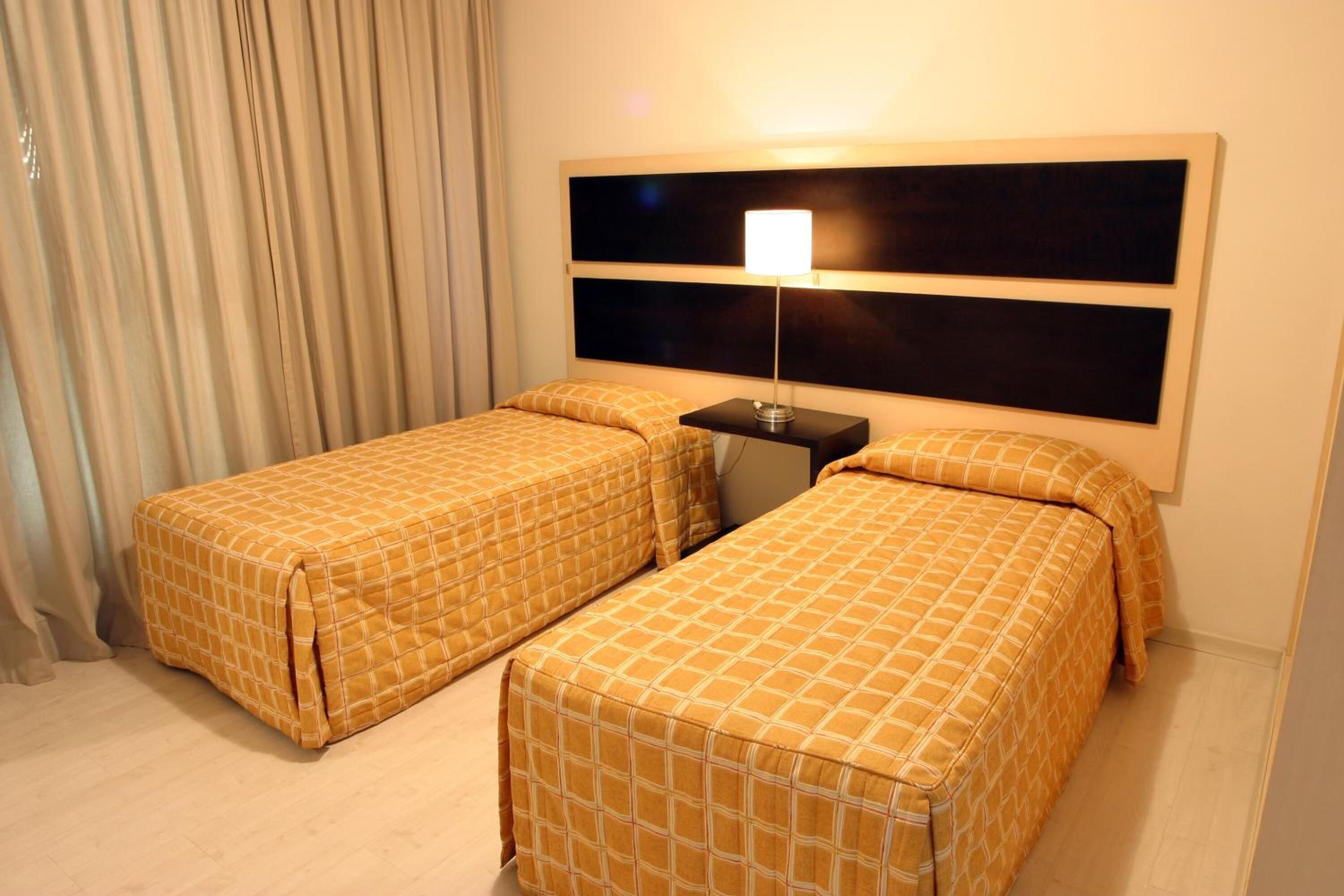 A hotel room with two single beds, a nightstand, and a large window with curtains.