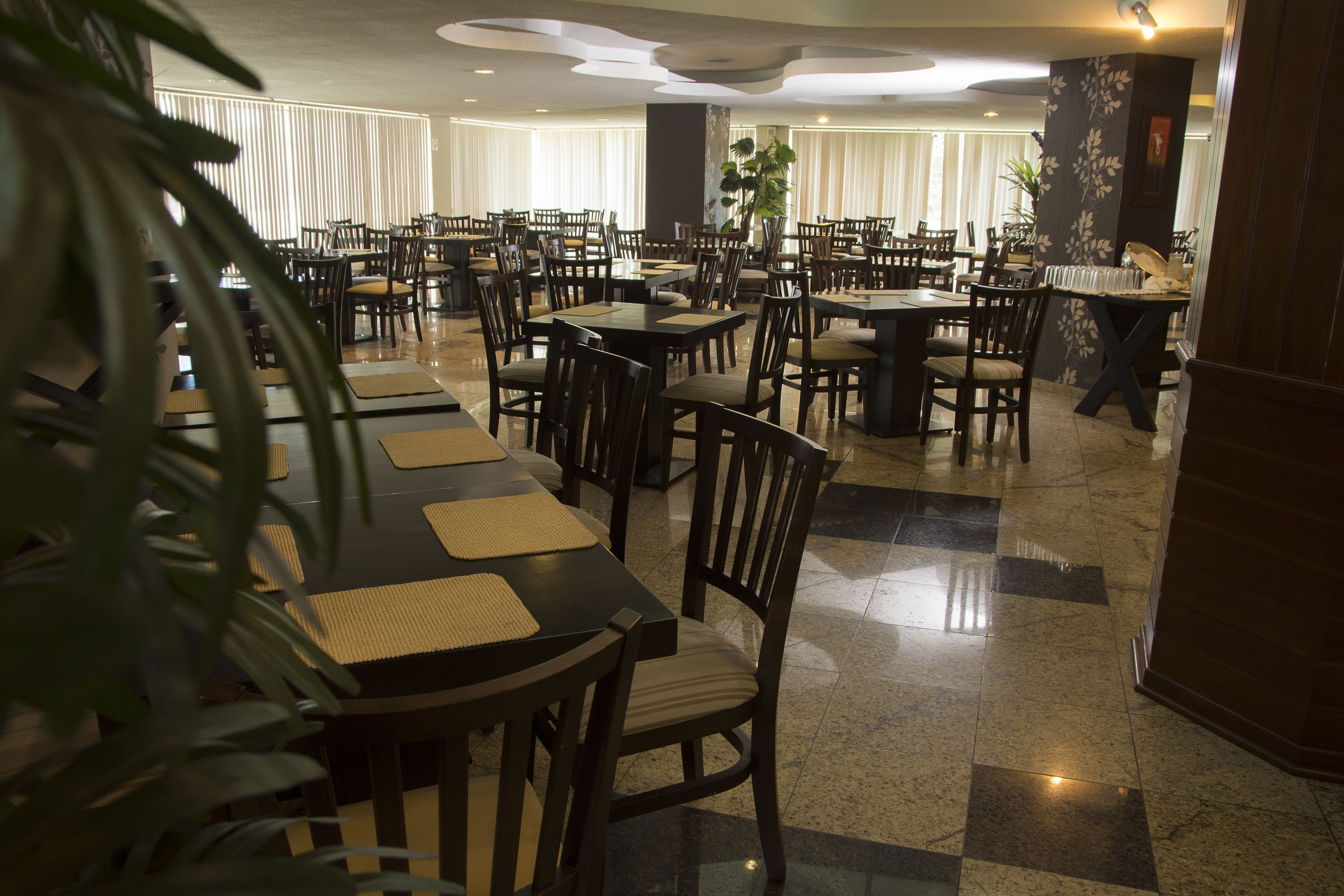 A spacious dining area with multiple tables and chairs, a polished tiled floor, and a large potted plant in the foreground.