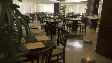 A spacious dining area with multiple tables and chairs, a polished tiled floor, and a large potted plant in the foreground.