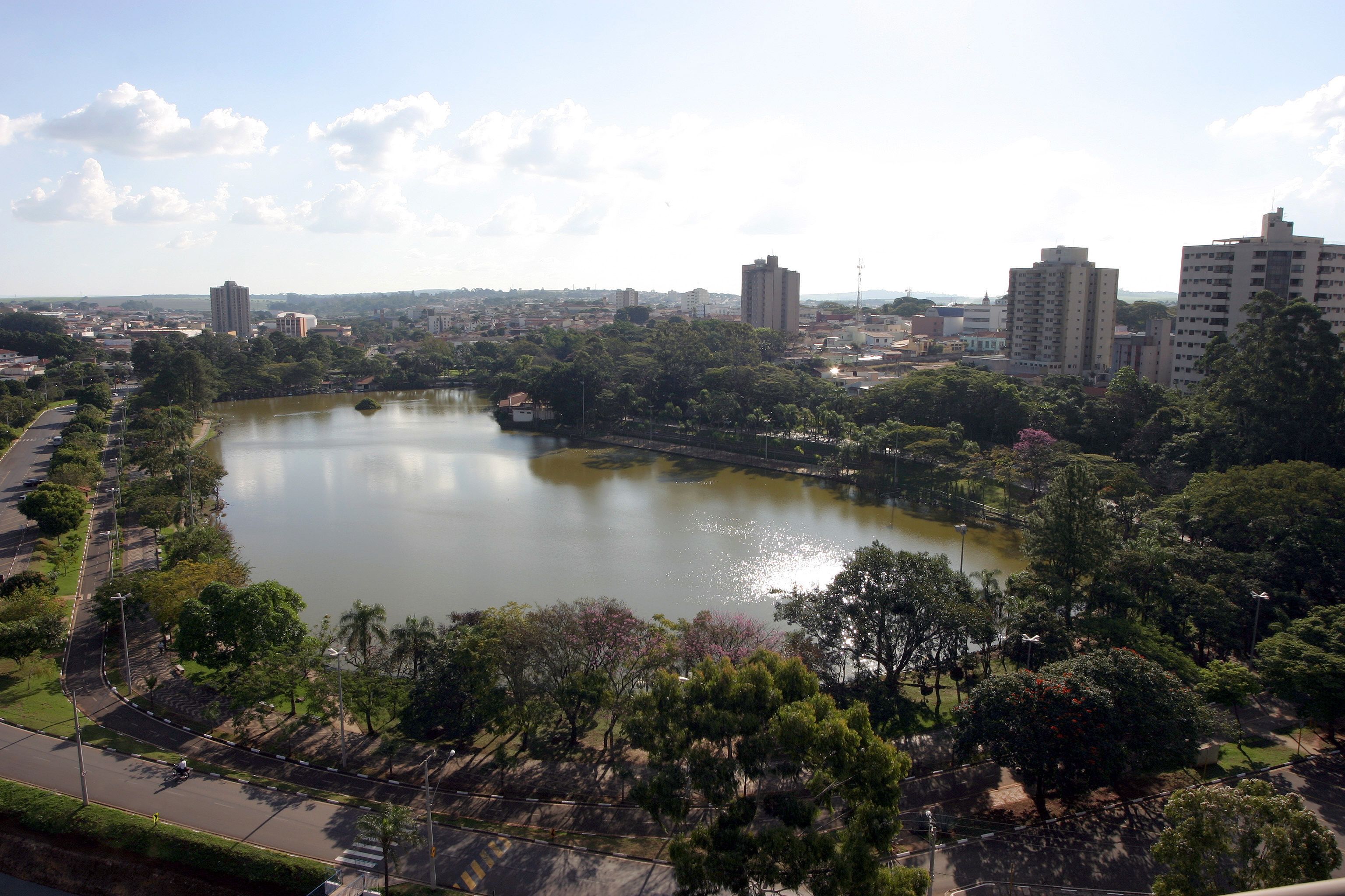 Un lago circondato da alberi e edifici, con una strada che costeggia la riva.