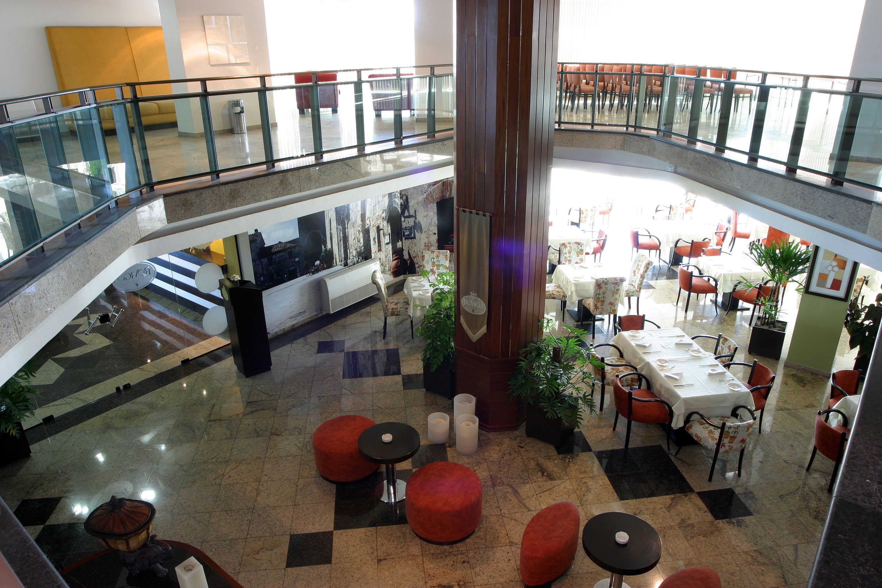Ein mehrgeschossiges Atrium mit Essbereich, roten Sitzgelegenheiten und einer Glasbrüstung, die auf die untere Ebene blickt.