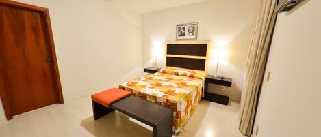 Un dormitorio con cama, banca, mesitas de noche y una puerta.