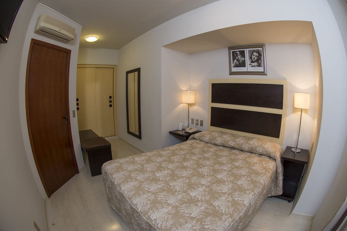 Un dormitorio con una cama grande, dos mesitas de noche con lámparas, un armario, un espejo y un equipo de aire acondicionado.