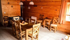 A wooden cabin interior with a dining table and chairs, a radiator, and a window with curtains. - Apart Hotel Tierra Nativa (San Martín de los Andes)