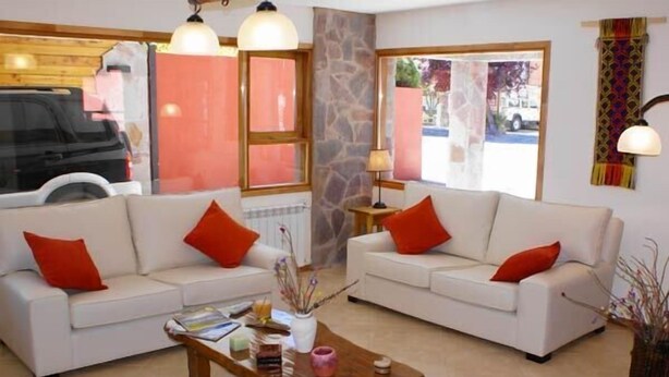 A living room with two white sofas, red cushions, a wooden coffee table, and a stone wall. - Apart Hotel Tierra Nativa (San Martín de los Andes)