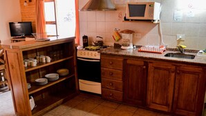 A compact kitchen with a stove, microwave, and sink. There are wooden cabinets and a shelf with plates. - Apart Hotel Tierra Nativa (San Martín de los Andes)