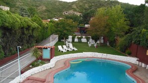 A swimming pool with a brick border, surrounded by a white stone wall, and a grassy area with lounge chairs. - Colonia Aoma Villa Carlos Paz (Villa Carlos Paz)