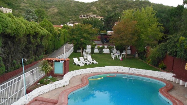 A swimming pool with a brick border, surrounded by a white stone wall, and a grassy area with lounge chairs. - Colonia Aoma Villa Carlos Paz (Villa Carlos Paz)