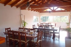 A spacious dining area with wooden tables and chairs, large windows, and ceiling fans. - Colonia Aoma Villa Carlos Paz (Villa Carlos Paz)