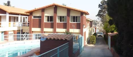 A two-story building with a swimming pool, a covered patio, and a car parked in the driveway.