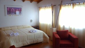 A bedroom with a large bed, a red armchair, and a window with curtains. - Colonia Aoma Villa Carlos Paz (Villa Carlos Paz)