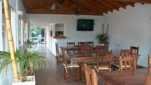 A dining area with wooden tables and chairs, a television mounted on the wall, and potted plants. - Colonia Aoma Villa Carlos Paz (Villa Carlos Paz)