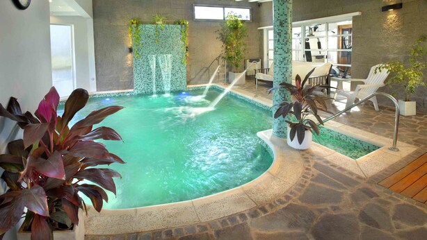Una piscina interior con suelo de piedra, una cascada y sillas de descanso.