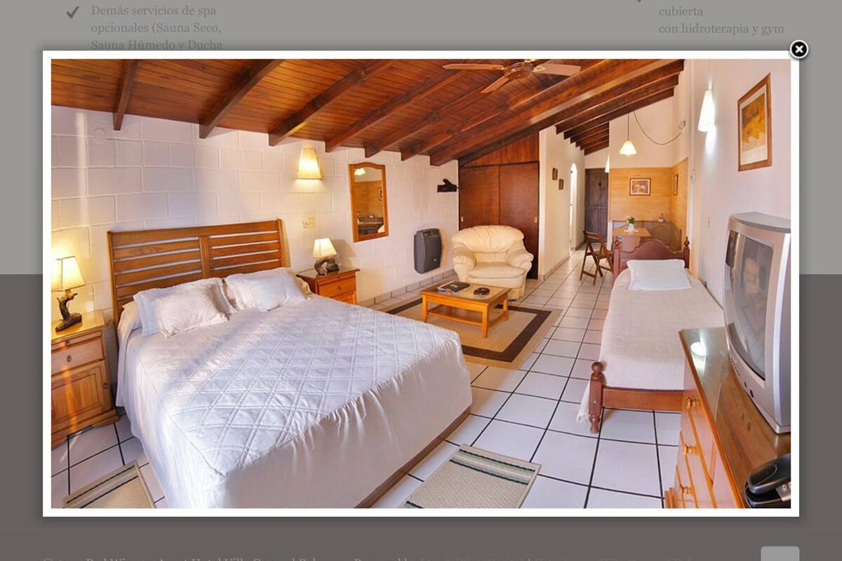 Un dormitorio amplio con una cama grande, techo de madera y televisor.