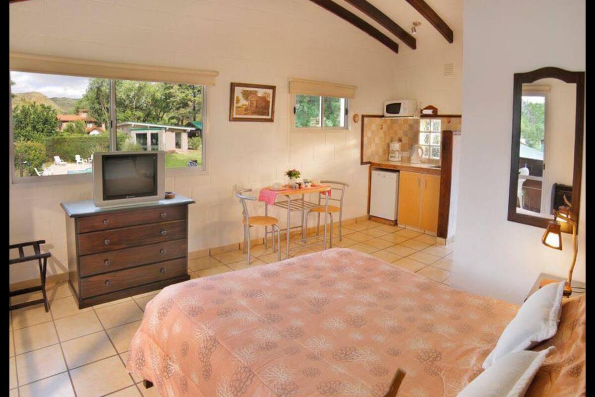 Un dormitorio con una cama grande, un aparador, un televisor, una mesa de comedor y una zona de cocina.
