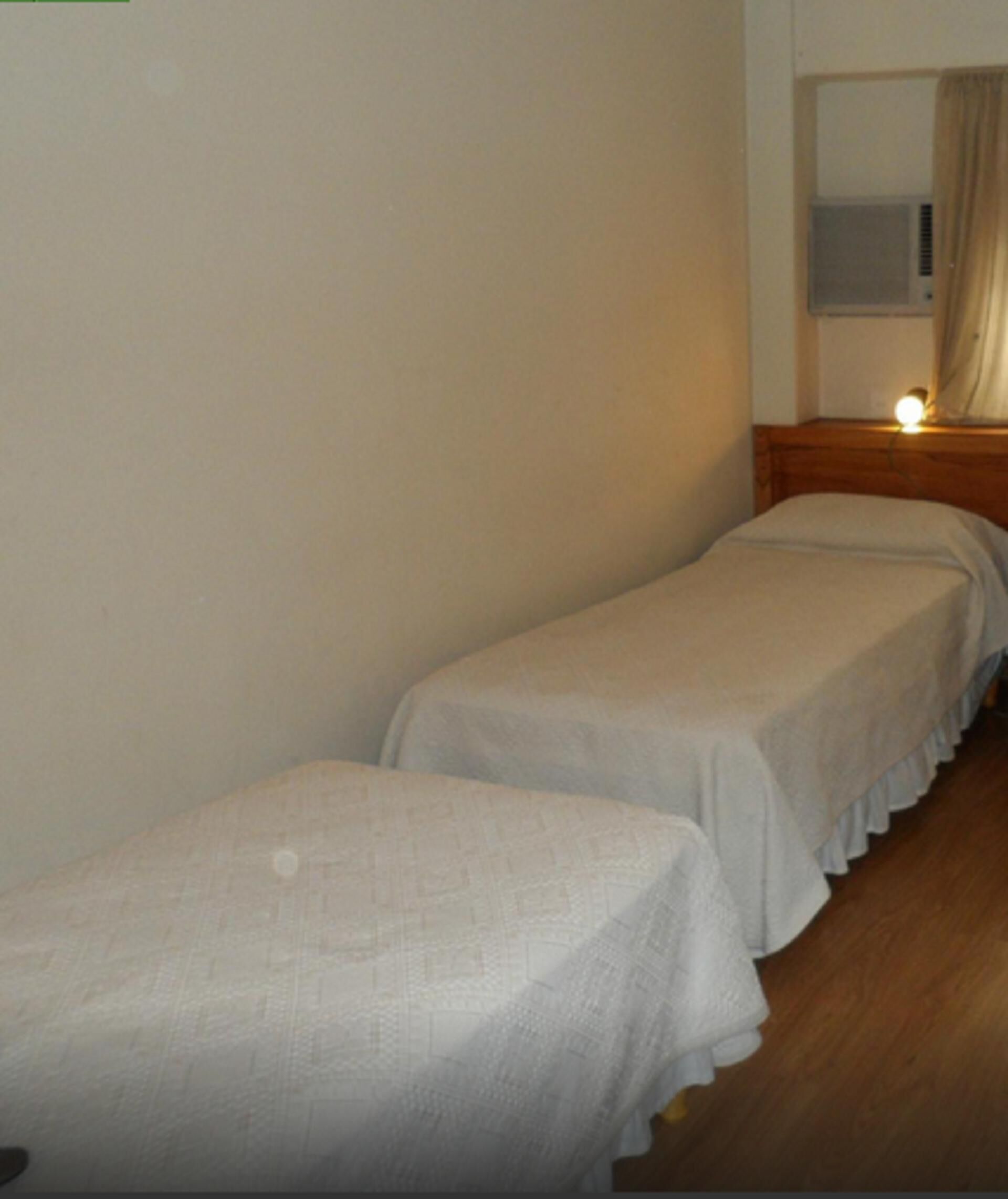 Una habitación pequeña y sencilla con dos camas individuales, suelo de madera y una ventana con cortinas.