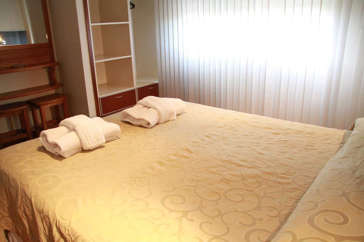 A hotel room with a neatly made bed, a wooden bench, a wardrobe, and a mirror.