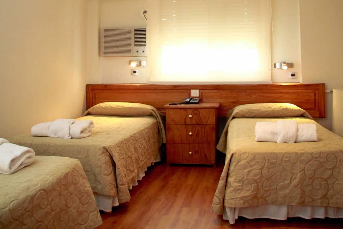 A hotel room with two single beds, each with a wooden headboard, a bedside table with a lamp, and a wall-mounted phone.