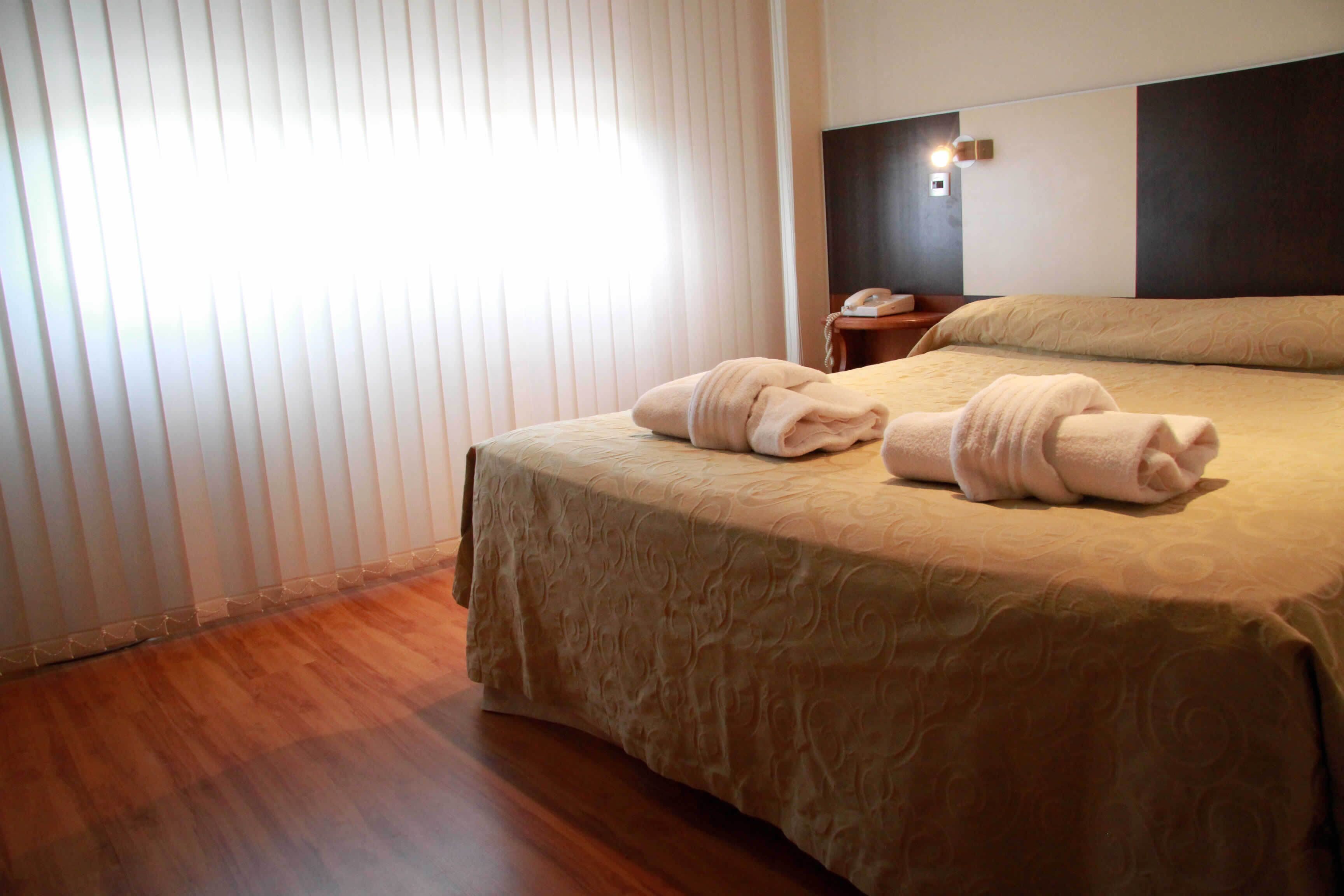 Una habitación de hotel con una cama grande, una mesita de noche con lámpara y una ventana con persianas.