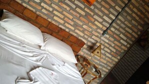 Une pièce avec un plafond orné d’un motif en briques, un lit recouvert de draps blancs et un tableau représentant un coucher de soleil.