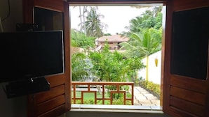 Une pièce avec une télévision sur le côté gauche, une fenêtre donnant sur un jardin et un bâtiment situé à l’extérieur.