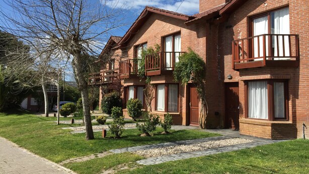 A row of brick townhouses with balconies, a paved pathway, and a grassy lawn. - Cabañas Madre Tierra (Valeria del Mar)