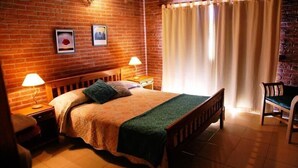 A cozy room with a brick wall, a bed with a green blanket, two bedside lamps, and a chair. - Cabañas Madre Tierra (Valeria del Mar)